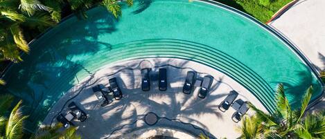 An aerial view of a resort with a large, curved swimming pool surrounded by lounge chairs and palm trees.