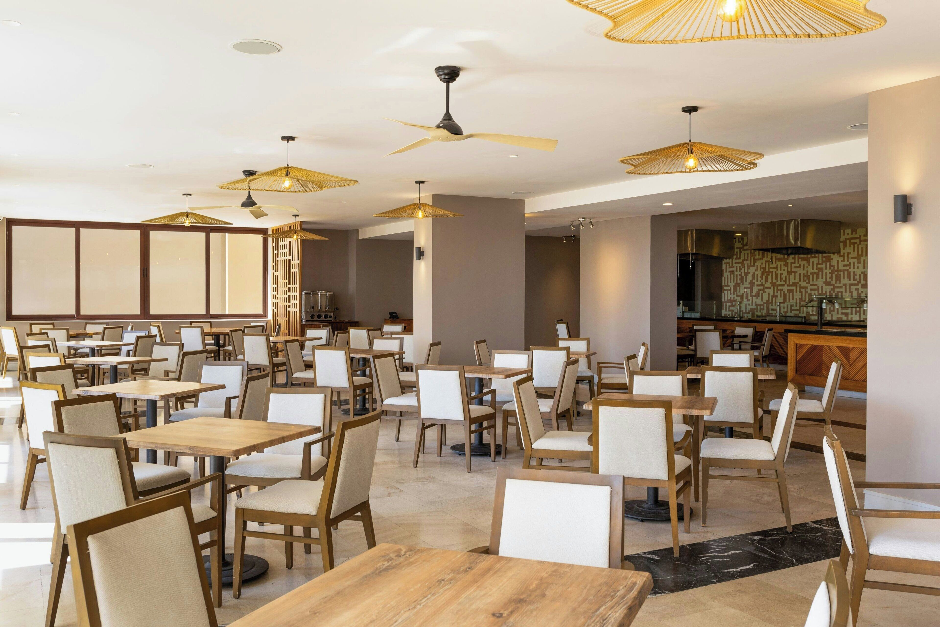 A spacious restaurant with multiple tables and chairs, ceiling fans, and pendant lights.