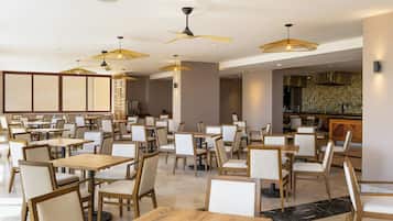 A spacious restaurant with multiple tables and chairs, ceiling fans, and pendant lights.