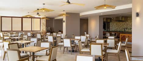 Ein großzügiges Restaurant mit mehreren Tischen und Stühlen, Deckenventilatoren und Pendelleuchten.
