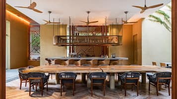 Ein geräumiger Essbereich mit einem großen Holztisch und Korbstühlen, eine Bar mit einer hohen Theke sowie Deckenventilatoren.