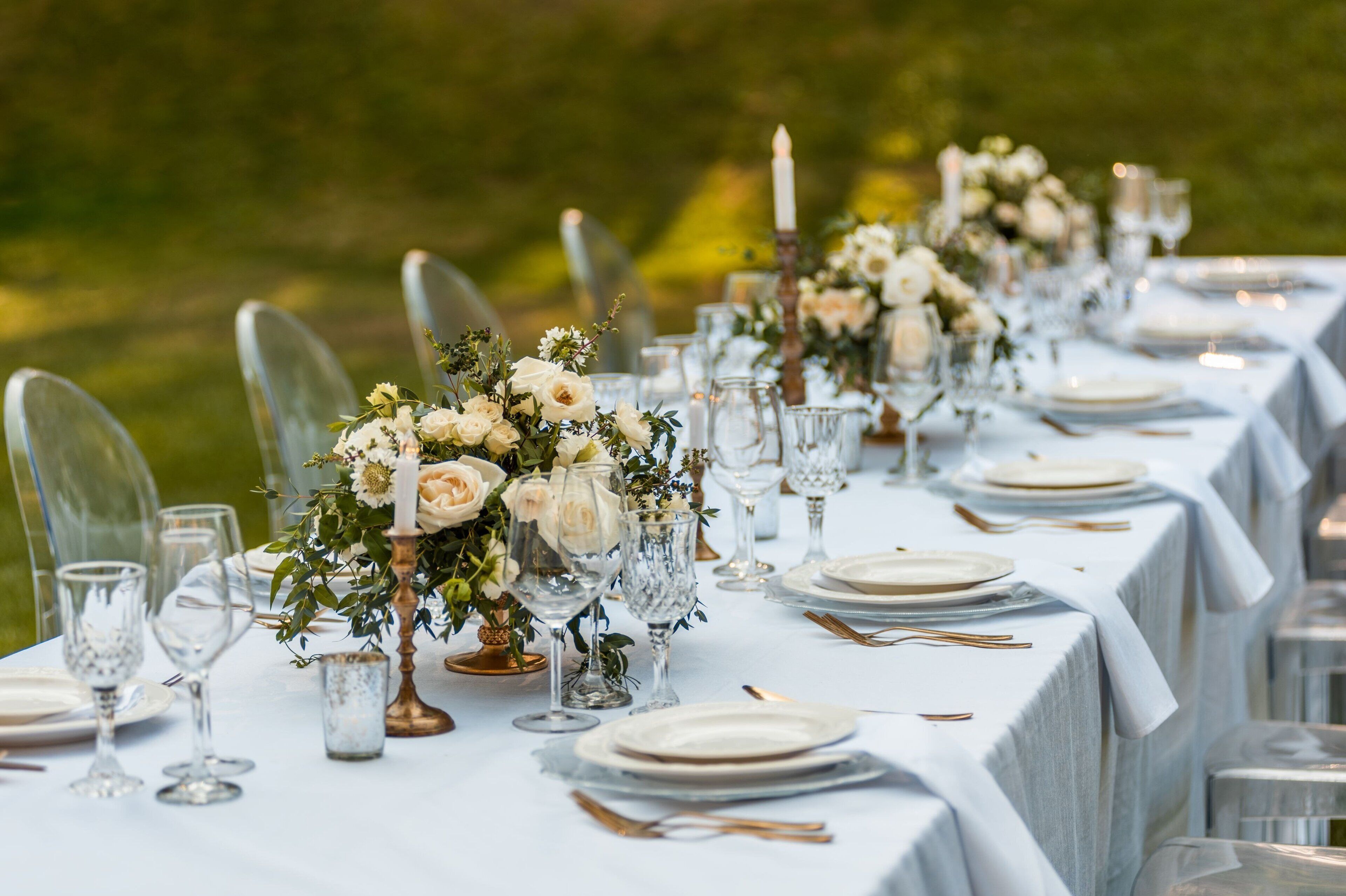 A long table set with white tablecloths, clear chairs, and floral centerpieces.
