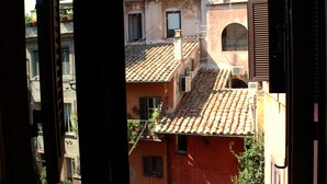 A view through a window of a building with a tiled roof, multiple windows, and balconies. - Abode of the Acetari in Campo de 'Fiori (Roma)