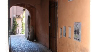 A cobblestone alleyway with an archway leading to a building. There are signs on the wall and a metal gate. - Abode of the Acetari in Campo de 'Fiori (Roma)