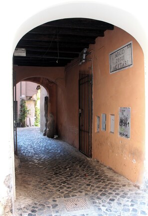 Une ruelle pavée, avec une arche menant à un bâtiment. On peut voir des panneaux sur le mur et une grille en métal.