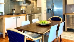 A modern kitchen with white cabinets, stainless steel appliances, and a wooden dining table with chairs. - Newly remodeled spacious 2bed/2bath with backyard in Willow Glen (San Jose)