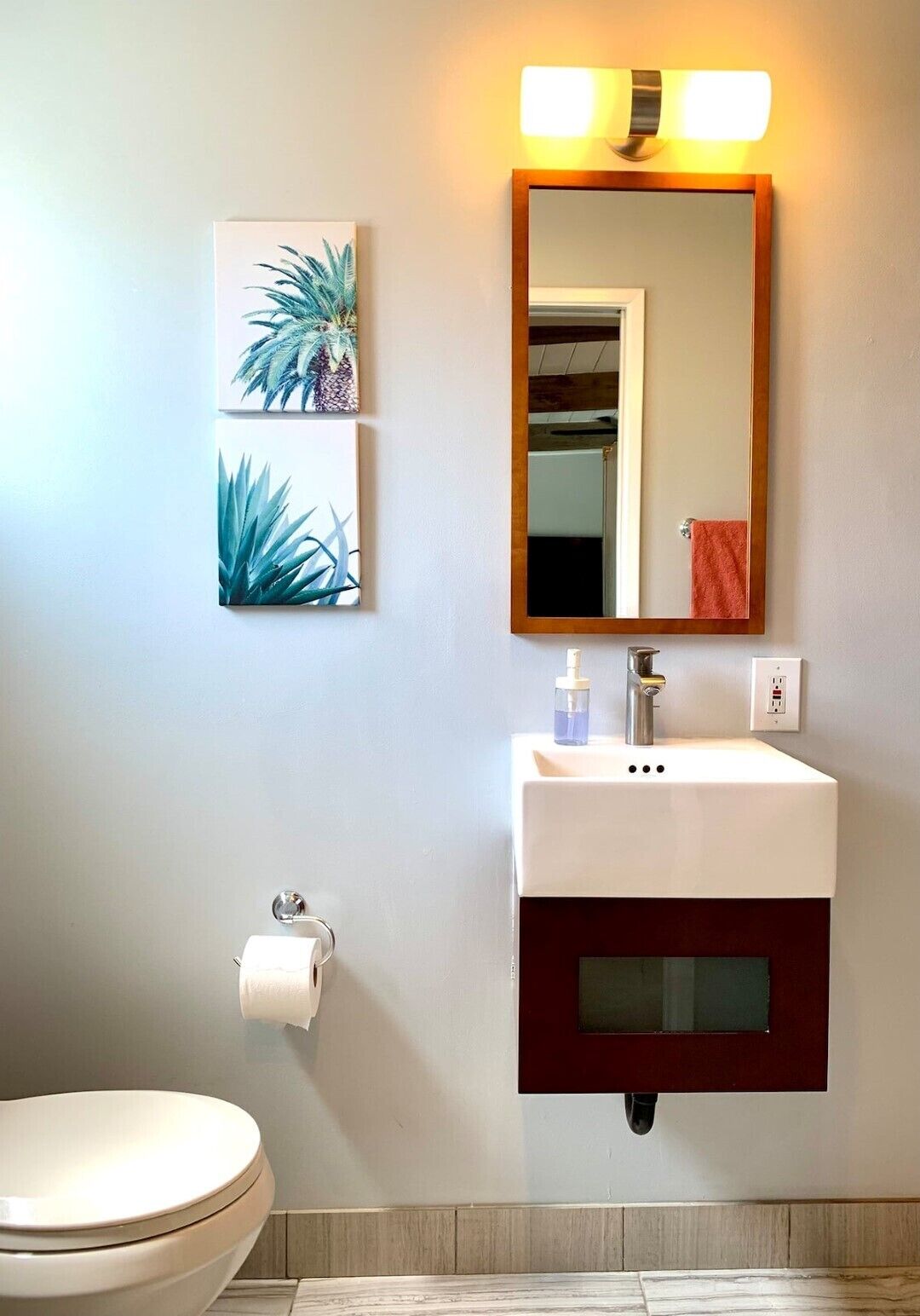 Ein Badezimmer mit einem weißen Waschbecken, einem Spiegel und zwei an der Wand befestigten Pflanzenbildern.