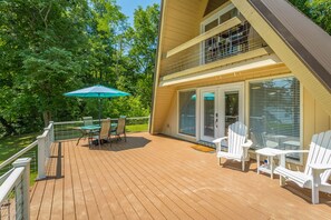 Een houten terras met tuinmeubilair, een overdekte zithoek en een glazen deur naar een balkon.