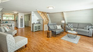 A spacious living area with a wooden floor, a grey sofa, patterned armchairs, a coffee table, and a staircase leading to an upper level. - The Tiger Lily - A PMI Scenic City Vacation Rental (Whitwell)