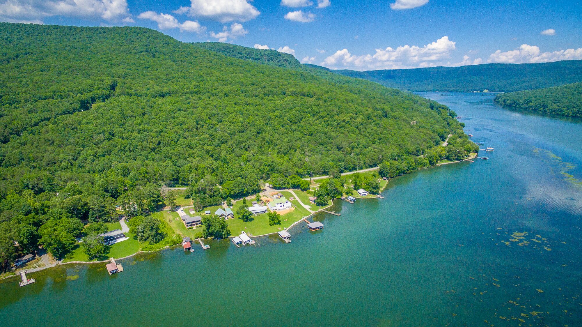 An aerial view of a lakeside property with multiple buildings, docks, and a forested hillside.