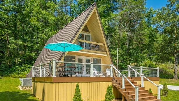 A two-story wooden cabin with a balcony, a staircase, and a covered outdoor seating area. - The Tiger Lily - A PMI Scenic City Vacation Rental (Whitwell)