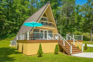 Een houten chalet met twee verdiepingen, een balkon, een trap en een overdekt terras.