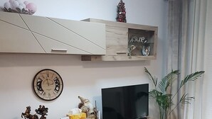 A modern living room with a flat-screen TV, wooden entertainment unit, decorative items, and a red ottoman. - Garsoniera Relax Rasnov (Râșnov Romacril)