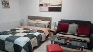 A modern bedroom with a bed, a sofa, a coffee table, and a red ottoman. - Garsoniera Relax Rasnov (Râșnov Romacril)