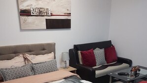 A modern bedroom with a large bed, a sofa, a small table, and a painting on the wall. - Garsoniera Relax Rasnov (Râșnov Romacril)