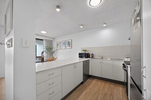 A modern kitchen with white cabinetry, a wooden floor, and recessed ceiling lights. - Ground Floor Apt 800m to Hastings Street & Beach (Noosa Heads)
