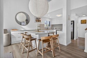 A modern kitchen with a central island, wooden chairs, and a hanging light fixture. - The River View - 10 min walk to Noosa Beach (Noosa Heads)