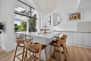 Eine moderne Küche mit einer zentralen Kochinsel, Holzbarhocker, einem großen Fenster und einer Pendelleuchte.