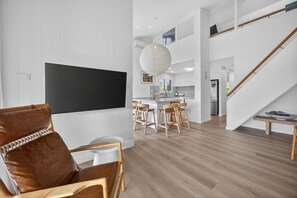 A modern living room with a flat-screen TV, a brown leather chair, a dining area with wooden chairs, a kitchen in the background, and a staircase. - The River View - 10 min walk to Noosa Beach (Noosa Heads)