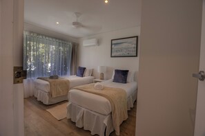 A bedroom with two beds, a ceiling fan, an air conditioning unit, a window with sheer curtains, and a framed picture on the wall. - Family First Floor Apt - 800m to Hastings Street! (Noosa Heads)