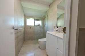 Une salle de bain moderne avec une douche à parois de verre, des toilettes blanches et un meuble-lavabo avec un miroir.