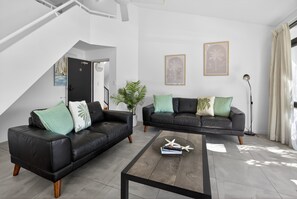 A modern living room with two black leather sofas, a coffee table, and a staircase. - Premium 3Bed Apt - Walking distance to Hastings St (Noosa Heads)