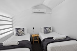 A small, white, single-room hotel room with two beds, a nightstand, a lamp, and a ceiling-mounted air conditioner. - Premium 3Bed Apt - Walking distance to Hastings St (Noosa Heads)