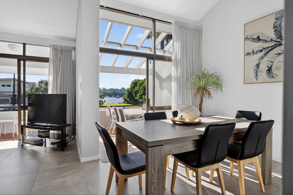A modern dining area with a large table, black chairs, and a TV on a stand.