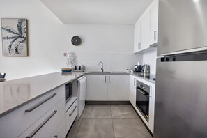 A modern kitchen with white cabinets, a stainless steel refrigerator, and a clock on the wall.