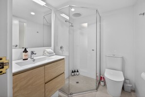 Une salle de bain moderne avec une douche à parois de verre, un lavabo blanc avec un miroir et des toilettes.
