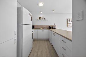 A modern kitchen with white cabinets, a wooden countertop, and a built-in oven. - Noosa Parade Escape - 800m to Hastings Street! (Noosa Heads)