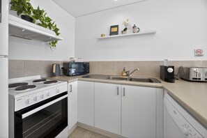 A modern kitchen with white cabinets, a built-in oven, a microwave, a coffee maker, and a toaster. - Noosa Parade Escape - 800m to Hastings Street! (Noosa Heads)