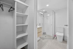 A modern bathroom with a glass shower enclosure, a white toilet, and a wooden vanity. - Noosa Parade Escape - 800m to Hastings Street! (Noosa Heads)