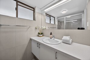 Un baño moderno con lavamanos, espejo y toallero blancos.