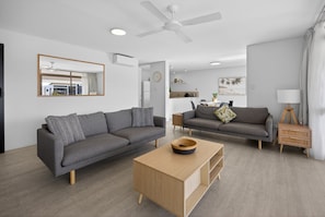 A modern living room with two sofas, a coffee table, and a dining area in the background. - Noosa Parade Escape - 800m to Hastings Street! (Noosa Heads)