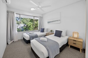 A hotel room with two beds, a ceiling fan, a window with curtains, a bedside table with a lamp, and a wall-mounted artwork. - Noosa Parade Escape - 800m to Hastings Street! (Noosa Heads)