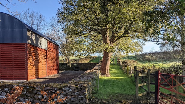 Propiedad rural con un granero rojo, muro de piedra y un camino de grava que lleva a una puerta de madera.
