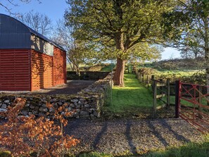 A rural property with a red barn, stone wall, and a gravel path leading to a wooden gate.