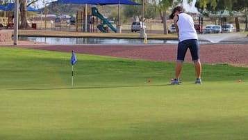 A golf course with a flag, a water feature, and a playground in the background.
