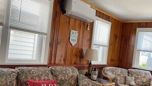 Ein Wohnzimmer mit zwei sofas in floralem Muster, einem roten Kissen, einer Wand-Klimaanlage und Holzdielen.