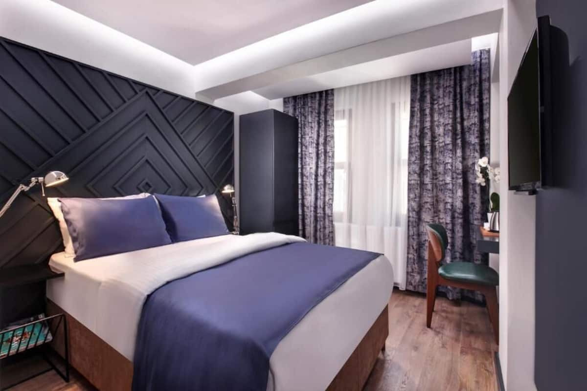 A modern hotel room with a large bed, a desk, a chair, and a TV.