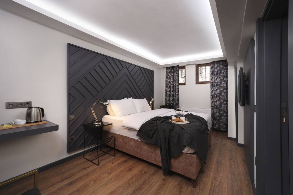 A modern bedroom with a bed, bedside table, lamp, and a wall-mounted shelf with a kettle.