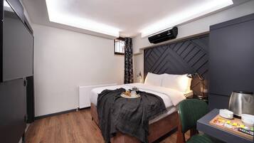 A hotel room with a bed, a desk with a chair, a radiator, a window with curtains, and a ceiling light.