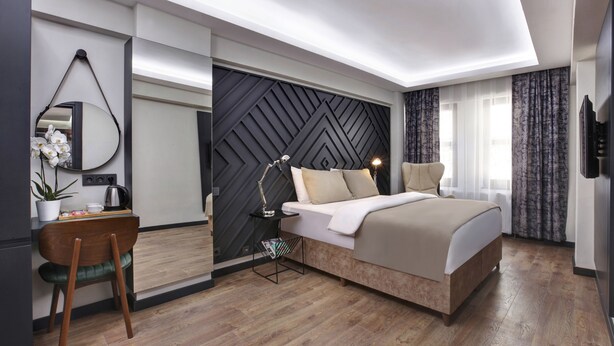 A modern bedroom with a bed, bedside table, lamp, and a decorative mirror. - Xenia Hotel Istanbul (Istanbul)