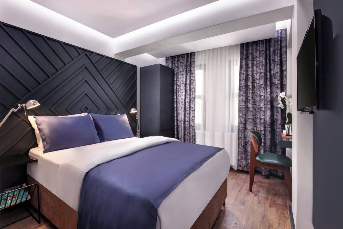 A modern hotel room with a large bed, a desk with a chair, and a TV mounted on the wall.
