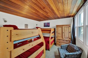 Una habitación con literas de madera, un armario y una silla estampada.