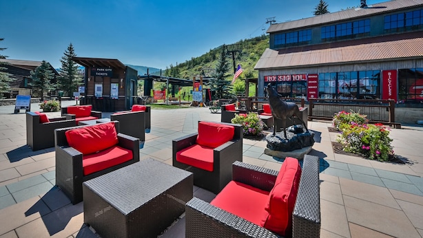 Un espace extérieur aménagé avec des meubles en osier et des coussins rouges, une statue et un bâtiment portant une enseigne indiquant un service de location de vélos.