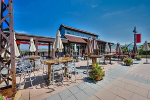 Dine al fresco at this outdoor patio, featuring tables and chairs under shaded umbrellas with a clear view of the building.