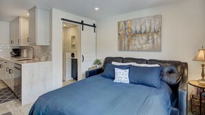 Quarto moderno com cama grande, escrivaninha e pequeno espaço de cozinha.