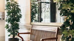 A wooden bench with a slatted backrest, positioned in front of a large mirror reflecting a window with metal bars. - Anakena House (Barcelona)